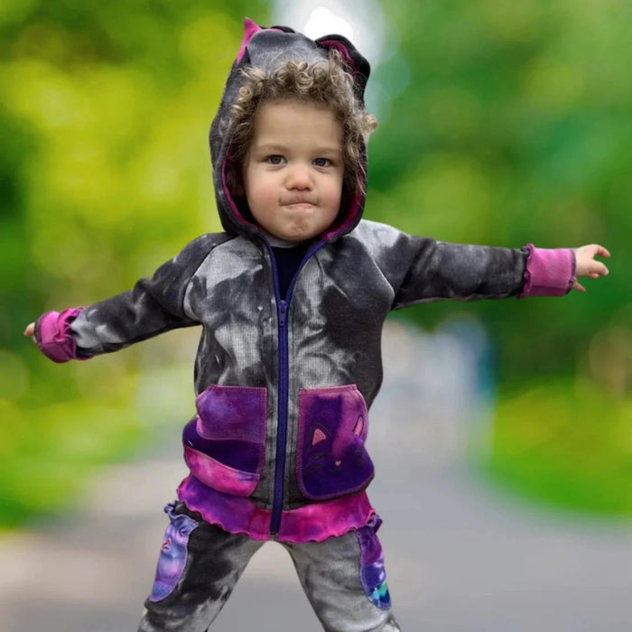 Child wearing a colorful hoodie and pants with arms outstretched on a blurred outdoor background
