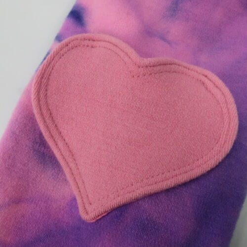 Bottom Additions- Heart Cargo Pocket. A cargo pocked in the shape of a heart that is lined in our lightweight merino wool. The heart has a double stitch around the outside. This pair has a pink heart on a purple/pink tie dye pants.