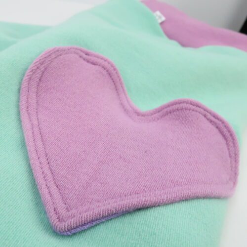Bottom Additions- Heart Cargo Pocket. A cargo pocked in the shape of a heart that is lined in our lightweight merino wool. The heart has a double stitch around the outside. This pair has a pink heart, matching the pink cuffs and waistband on a light green pants.